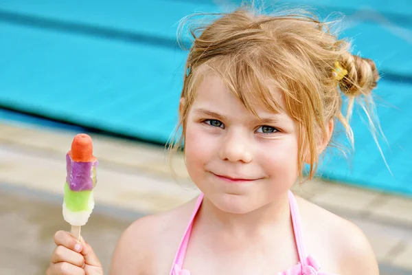 可爱而快乐的小女孩在游泳池里喝水后吃着冰棒冰淇淋 — 图库照片