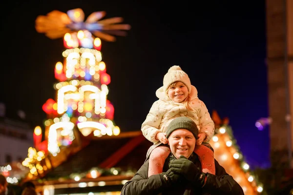 在德国的圣诞市场上 幼儿园的小女孩坐在父亲的肩上 快乐的幼儿和男人观察着传统的装饰金字塔 快乐的家庭 亲密的感情 家庭圣诞节时间 — 图库照片