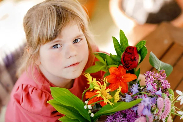 自宅で花の花束を持つ小さな就学前の女の子 幼児の子供は水と小さなボトルにカラフルな庭の夏の花を入れます 子供のためのホームアクティビティ 虹色の花 幸せな子供 — ストック写真