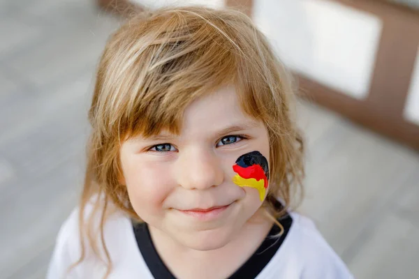 Little blond preschool girl watching soccer football cup game on public viewing. Happy joyful excited child about winning game match of favorite national football team. girl with German flag on face