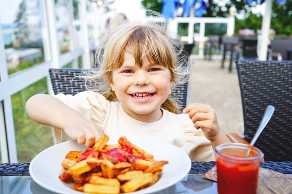 テラスの屋外レストランでトマトケチャップでフレンチフライを食べる幸せな笑顔の就学前の少女の肖像画 金髪の小さな子供は不健康なファーストフードや新鮮な準備されたランチを楽しむ — ストック写真