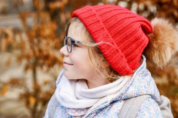 眼鏡と赤い帽子を屋外でかわいい就学前の女の子の肖像画 新しい青い眼鏡をかけて幸せな面白い子供 市内の秋の日 — ストック写真