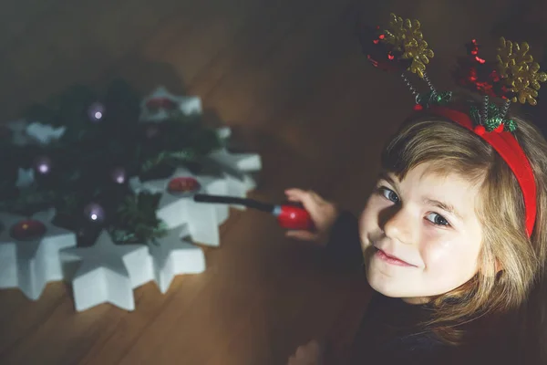 圣诞节前夕或第一次来临时 带着可笑的圣诞头巾的学龄前小女孩在来临时点燃一支蜡烛 德国的传统花环 快乐的孩子庆祝家庭节日 — 图库照片