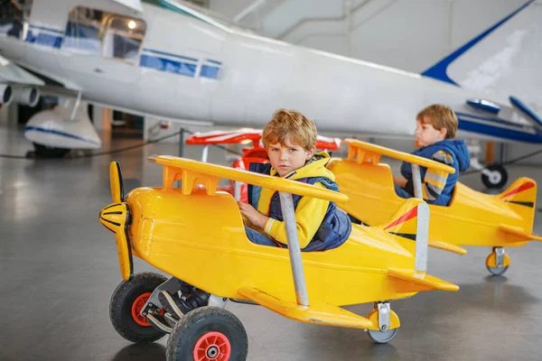 两个小男孩开着老式的大玩具踏板飞机 在屋里玩得很开心 学校放假期间与子女一起积极休闲活动 — 图库照片
