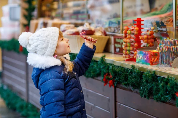 クリスマスマーケットのお菓子スタンドからお菓子を買うかわいい就学前の女の子 ドイツの伝統的な家庭市場で幸せな子供 カラフルな冬服の就学前 — ストック写真