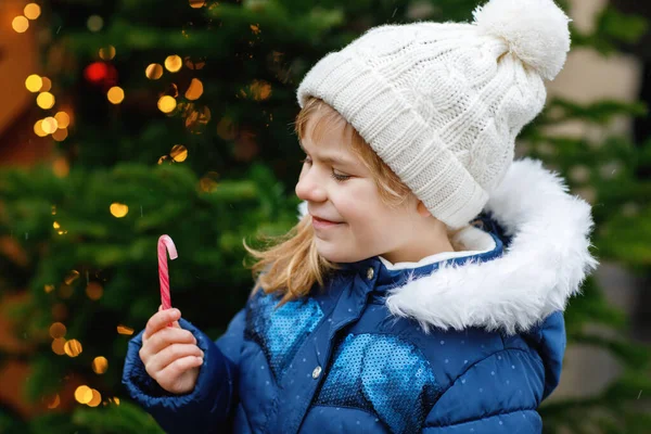 圣诞节市场上站着一个可爱的学龄前小女孩 手里拿着糖果手杖 德国传统家庭市场上的快乐孩子 大雪中穿着五颜六色冬衣的学龄前儿童 — 图库照片
