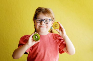 Happy little child girl with yellow and green kiwi fruits on yellow background. Preschool girl smiling. Healthy fruits for children.