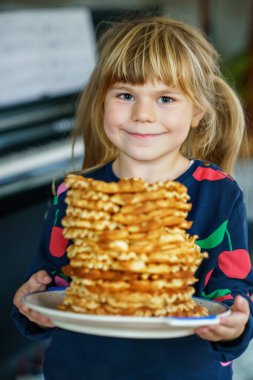 Anaokulundaki küçük mutlu kızın portresi elinde taze waffle tutuyordu. Tatlı bisküvi ekmeğiyle gülümseyen aç bir çocuk. Tatlı Belçika waffle 'ları