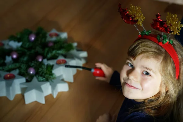 Kis Óvodás Lány Vicces Karácsonyi Fejpánttal Gyertyát Gyújt Adventi Koszorún — Stock Fotó