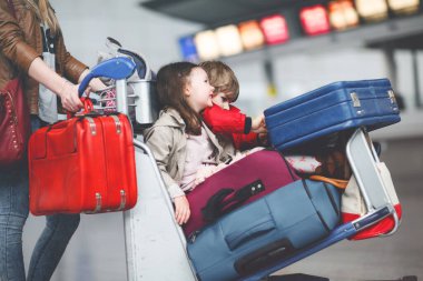 İki küçük çocuk, erkek ve kız, kardeşler ve anne havaalanında. Çocuklar, aile seyahati, uçakla tatile gitmek ve bir kadının terminalden uçmak için ittiği valizlerle tramvayda beklemek.