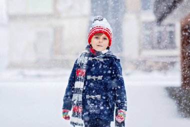 Renkli elbiseli anaokulu çocuğu şiddetli kar yağışı sırasında dışarıda oynuyor. Soğuk karlı günlerde, kışın çocuklarla aktif eğlence. Mutlu çocuk eğleniyor, karla oynuyor. Kış modası