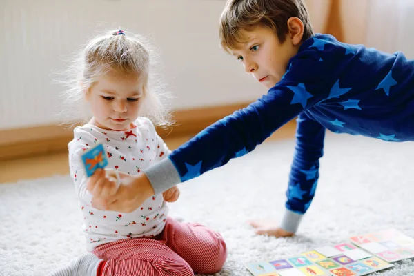 两个小孩 可爱的蹒跚学步的小女孩和学童在装饰圣诞树旁玩纸牌游戏 祝你兄弟姐妹健康 兄弟姊妹在一起玩得开心 庆祝圣诞节的家庭 — 图库照片