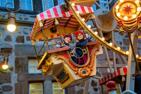 在户外的圣诞游乐场或市场上 学龄前小女孩和学童骑着摩天轮旋转木马 两个快乐的孩子在德国传统的家庭圣诞市场上玩得很开心 — 图库照片