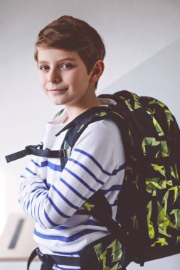 Okul çantalı güzel çocuk sabahın erken saatlerinde odada duruyor. Okula ve derslere giden mutlu sağlıklı çocuk. Eğitim kavramı.