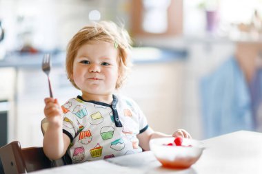 Kaşık dolusu sağlıklı ahududu, çocuk, beslenme ve gelişim kavramından beslenen sevimli bir kız bebek. Sevimli bebek, kaşıklı kız sandalyede oturuyor ve kendi kendine yemek yemeyi öğreniyor.