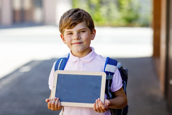 Happy little kid boy with backpack or satchel. Schoolkid on the way to school. Healthy adorable child outdoors On desk Last day second grade in German. Schools out.
