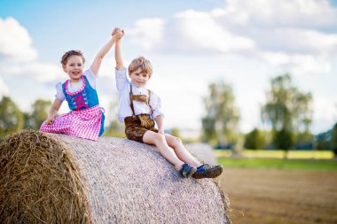Buğday tarlasında geleneksel Bavyera kostümlü iki çocuk. Alman çocukları Ekim Festivali sırasında saman balyasında oturuyorlar. Almanya 'da yaz aylarında erkek ve kız saman balyalarında oynarlar. En iyi arkadaşlar