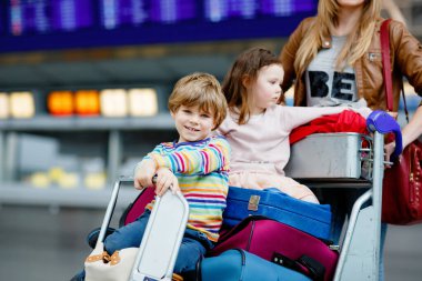 İki küçük çocuk, erkek ve kız, kardeşler ve anne havaalanında. Çocuklar, aile seyahati, uçakla tatile gitmek ve bir kadının terminalden uçmak için ittiği valizlerle tramvayda beklemek.