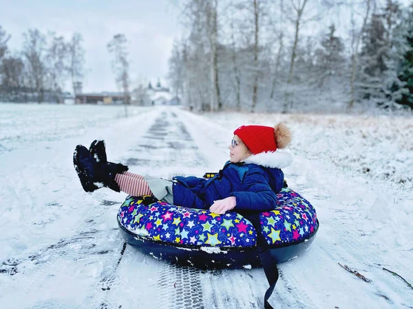 Active prechool girl sliding down the hill on snow tube. Cute little happy child having fun outdoors in winter on sledge . Healthy excited kid tubing snowy downhill, family winter time