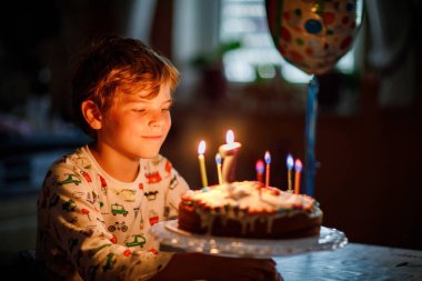 Sevimli, mutlu, küçük sarışın çocuk doğum gününü kutluyor. Çocuk ev yapımı pastaya yedi mum üflüyor. Okul çocukları için doğum günü partisi, 7 yıllık aile kutlaması..