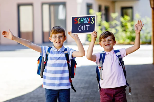 リュックかサッチェルを持った2人の子供 学校に行く途中の子供たち 健康な子供たちは 兄弟や親友屋外の通りに家を出る チョーク デスクで学校だ 幸せな兄弟たち — ストック写真