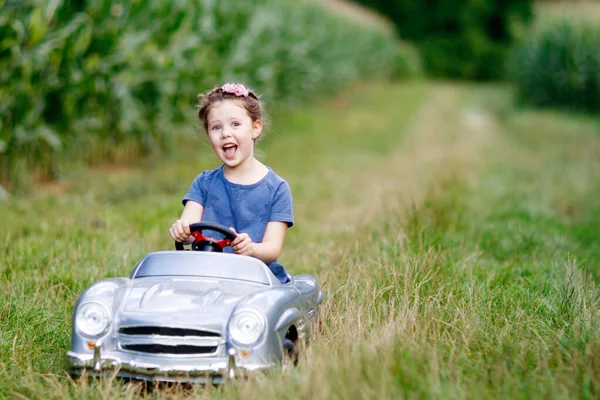 小さな就学前の子供の女の子は大きなヴィンテージの古いおもちゃの車を運転し トウモロコシ畑 屋外で楽しい運転をしています 自然の風景の中で暖かい夏の日を楽しむ子供 女の子の運転車 — ストック写真