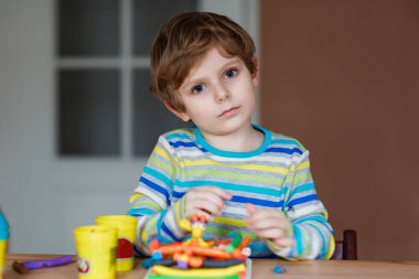 Gülümseyen anaokulu çocuğu hamurla eğleniyor, renkli modelleme bileşik kiliyle. Çocuklarla yaratıcı bir eğlence. Corona virüsü karantinası sırasında evde kalmak. Sığınma yeri, tecrit kavramı