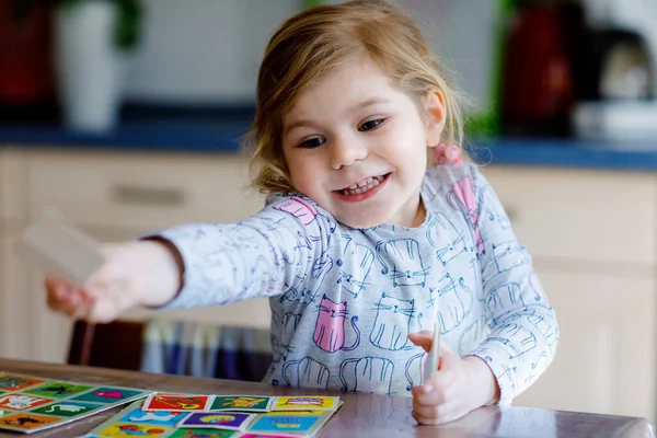 Excited smiling cute toddler girl playing picture card game. Happy healthy child training memory, thinking. Creative indoors leisure and education of kid. Family activity at home