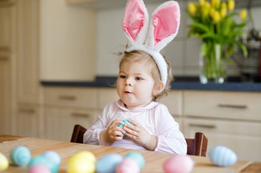 Paskalya tavşanı kulakları takan tatlı küçük kız renkli pastel yumurtalarla oynuyor. Mutlu bebek hediyeleri açıyor. Pembe elbiseli sevimli, sağlıklı çocuk aile tatilinin tadını çıkarıyor.,