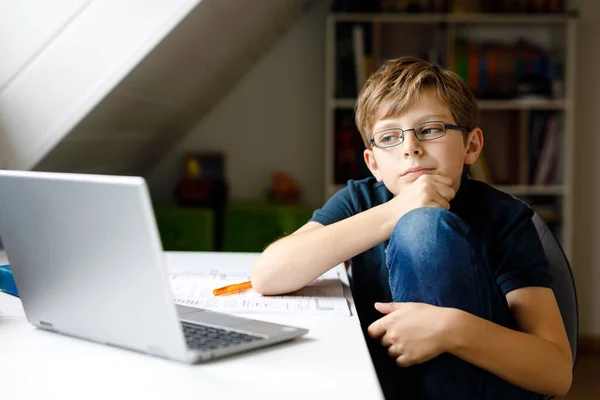 Kid boy with glasses learning at home on laptop for school. Adorable child making homework and using notebook and modern gadgets. Home schooling concept