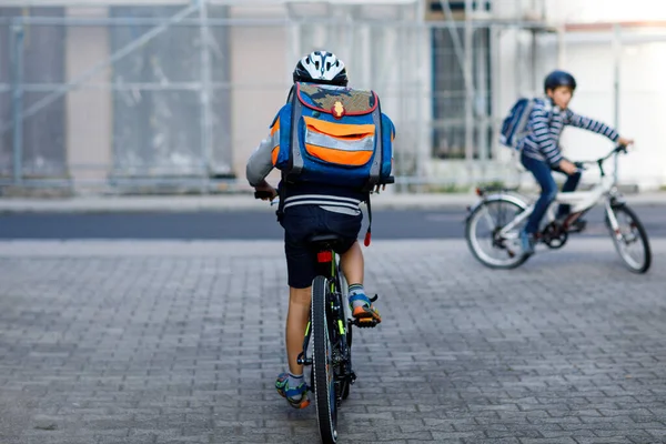 市内の自転車にバックパックで乗っている安全ヘルメットに乗っている2人の子供の男の子 学校に行く途中で自転車に乗ってカラフルな服を着た幸せな子供たち 学校への屋外の子供のための安全な方法 — ストック写真