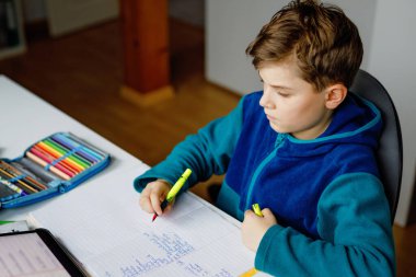 Okul çocuğu evde okul için tabletle öğreniyor. Ev ödevi yapan, ped kullanan ve modern aletler kullanan sevimli bir çocuk. Evde eğitim ve uzaklık öğrenme kavramı