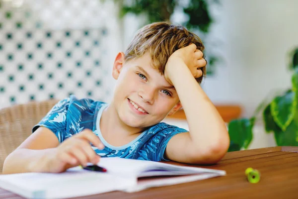Hard-working happy school kid boy making homework during quarantine time from corona pandemic disease. Healthy child writing with pen, staying at home. Homeschooling concept.