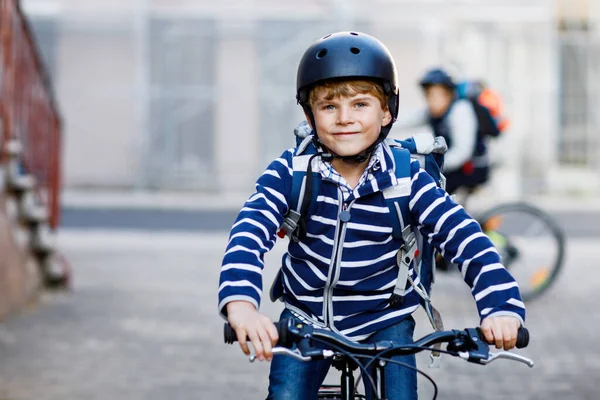 市内の自転車にバックパックで乗っている安全ヘルメットに乗っている2人の子供の男の子 学校に行く途中で自転車に乗ってカラフルな服を着た幸せな子供たち 学校への屋外の子供のための安全な方法 — ストック写真