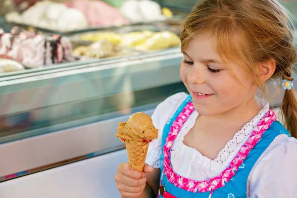 Little preschool girl eating sweet ice cream in waffle cone on sunny summer day. Happy toddler child eat icecream dessert. Sweet food on hot warm summertime days.