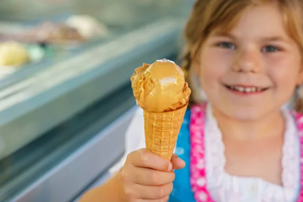 Little preschool girl eating sweet ice cream in waffle cone on sunny summer day. Happy toddler child eat icecream dessert. Sweet food on hot warm summertime days.