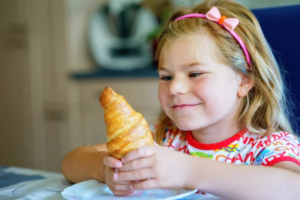 朝食で笑顔の子供 食べ物と幸せな子供たち 少女はクロワッサンを食べている 可愛いです就学前の女の子持っている健康的な食事 — ストック写真