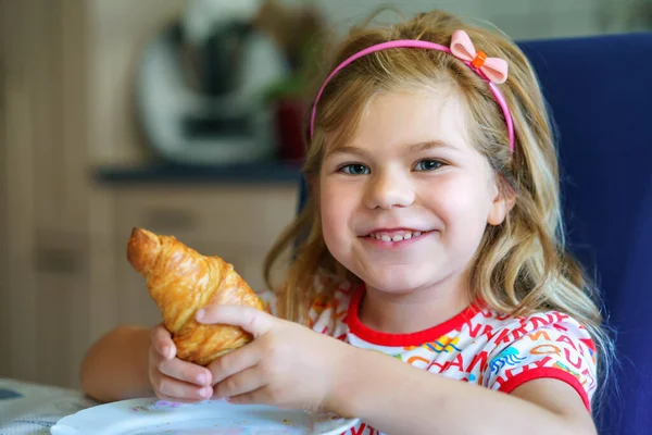 Smiling child at breakfast. Food and happy kids. The girl is eating a croissant. Cute preschool girl having healthy meal