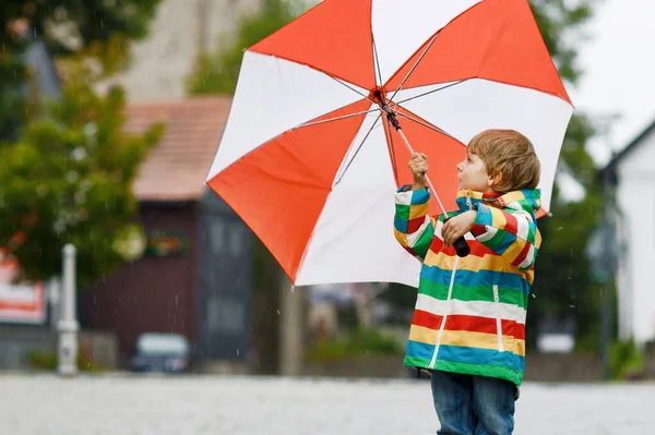 雨の日に大きな傘で遊んでいる小さな幼児の少年 雨や水たまりの中を走る幸せな正の子 雨の服やゴムブーツを持つ子供 悪天候の日の子供たちの屋外活動 — ストック写真