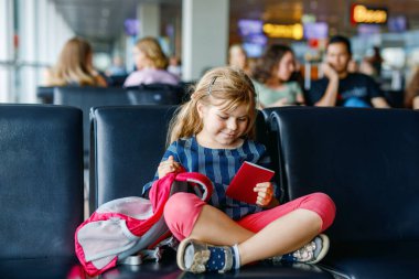 Küçük kız havaalanında büyük pencerede biniş için bekliyor. Pasaportu olan sevimli bir çocuk yaz tatiline gitmeyi dört gözle bekliyor..