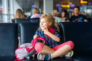 Küçük kız havaalanında büyük pencerede biniş için bekliyor. Pasaportu olan sevimli bir çocuk yaz tatiline gitmeyi dört gözle bekliyor..