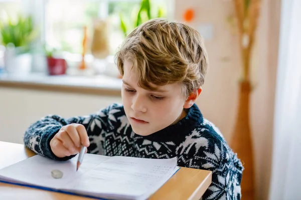 Hard-working happy school kid boy making homework during quarantine time from corona pandemic disease. Healthy child writing with pen, staying at home. Homeschooling concept.