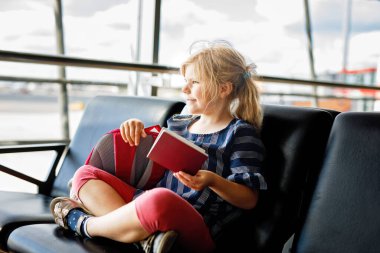 Küçük kız havaalanında büyük pencerede biniş için bekliyor. Pasaportu olan sevimli bir çocuk yaz tatiline gitmeyi dört gözle bekliyor..
