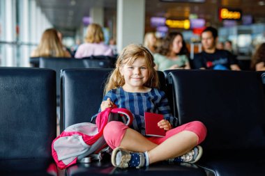 Küçük kız havaalanında büyük pencerede biniş için bekliyor. Pasaportu olan sevimli bir çocuk yaz tatiline gitmeyi dört gözle bekliyor..