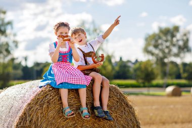 Buğday tarlasında geleneksel Bavyera kostümlü iki çocuk. Alman çocukları Ekim Festivali sırasında ekmek ve simit yiyorlar. Almanya 'da yaz aylarında erkek ve kız saman balyalarında oynuyorlar.