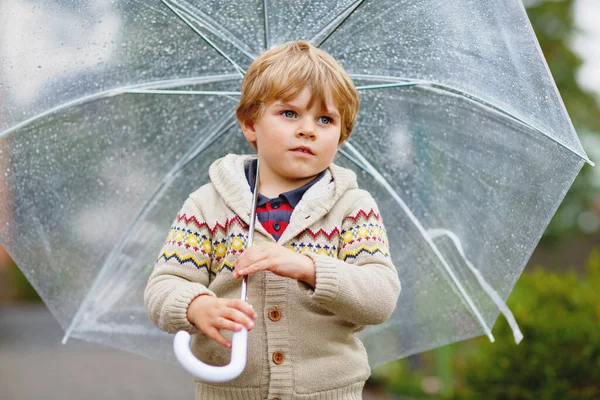 小さな金髪の少年は雨の日に大きな傘を屋外で歩いています 楽しいカラフルな防水服を着ているかわいい就学前の子供の肖像画 屋外レジャー子供と悪天候の日に歩く — ストック写真
