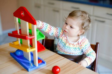 Küçük kız evde ya da çocuk odasında eğitici oyuncaklarla oynuyor. Mutlu sağlıklı çocuk renkli tahta top pisti ile eğleniyor. Çocuk top tutmayı ve yuvarlanmayı öğreniyor. Motorik eğitim