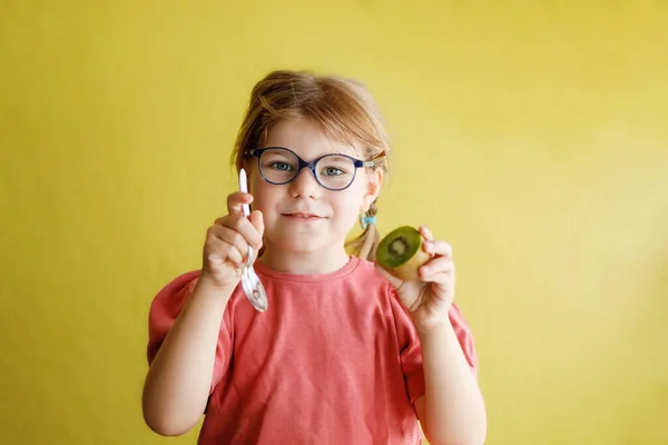 Szczęśliwa Dziewczynka Okularach Jedząca Owoce Kiwi Łyżeczką Żółtym Tle Uśmiechnięta — Zdjęcie stockowe
