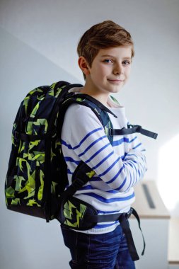 Okul çantalı güzel çocuk sabahın erken saatlerinde odada duruyor. Okula ve derslere giden mutlu sağlıklı çocuk. Eğitim kavramı.