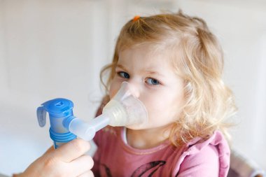 Küçük kız evde nebulizörle nefes alıp veriyor. Baba ya da anne yardım ediyor ve cihazı tutuyor. Çocuk grip, öksürük ve bronşit olmuş. Astım spreyi soluması buhar tutması konsepti.